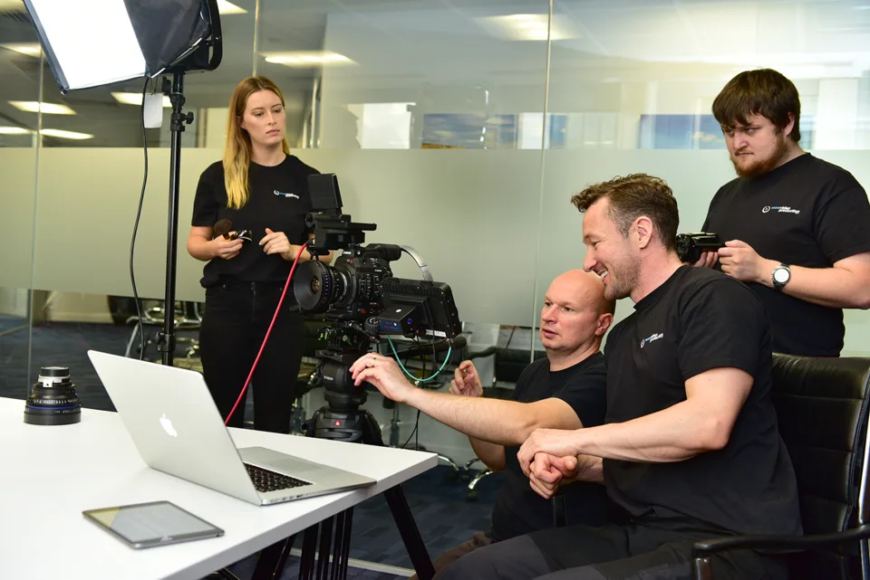 Video-production crew operating a camera beside a laptop.